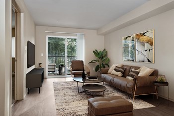 Living room with sliding glass door to the balcony on the far wall, matching chair, couch, and ottoman with a table in the center across from a tv and entertainment unit